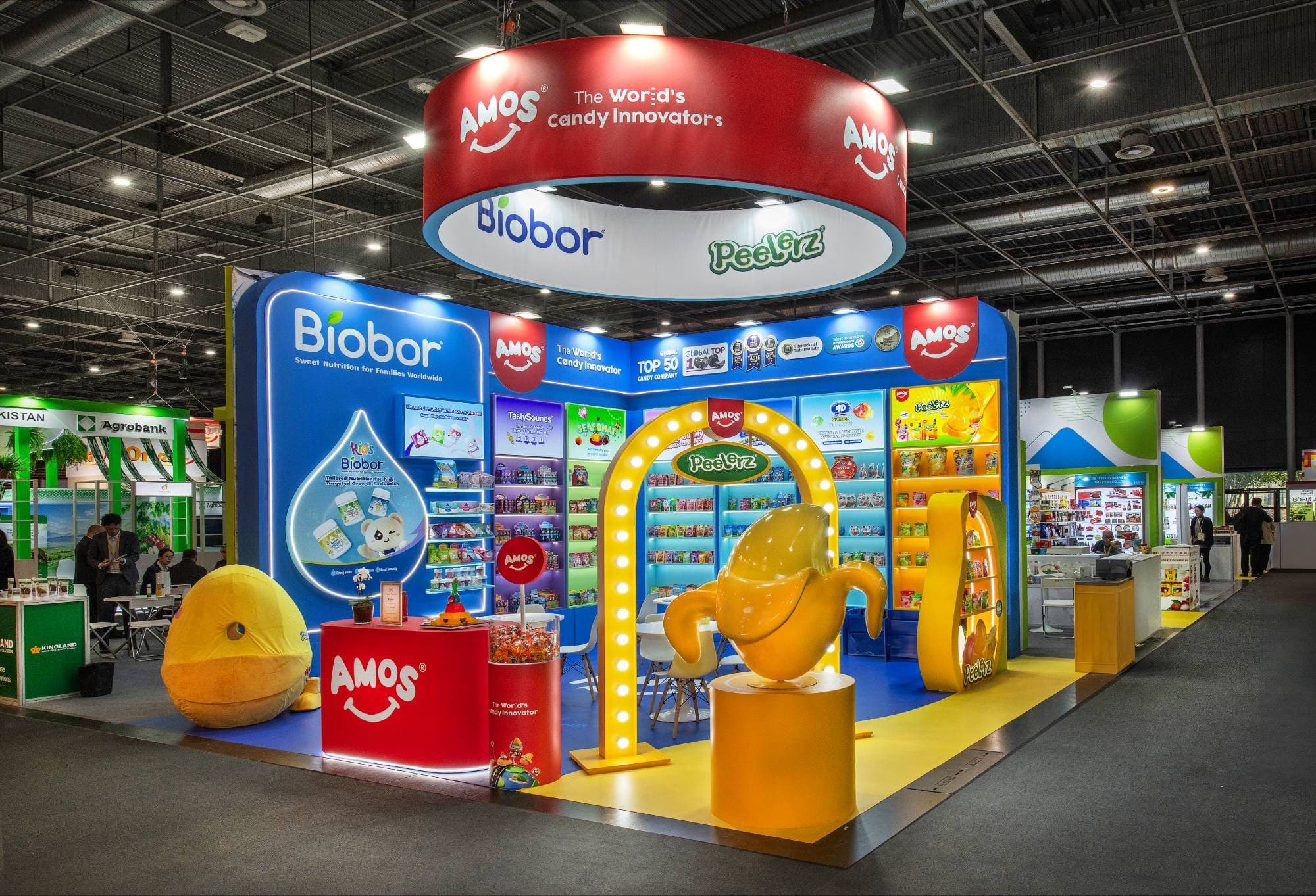 Stand Biobor de 36 m² au SIAL Paris 2026 : cloison bleue rétroéclairée, arche jaune à ampoules, banane géante Peelerz et linéaires lumineux de bonbons